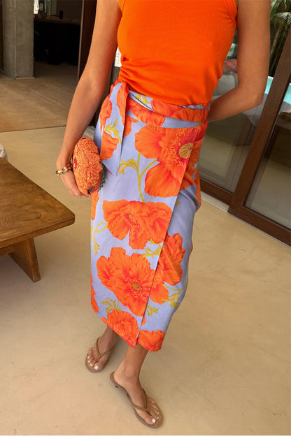 Blue Poppy Jaspre Skirt with orange floral print and wrap tie, styled with an orange top and beaded clutch.