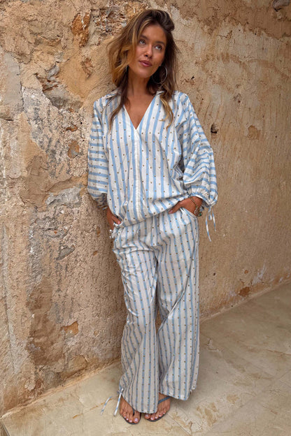 Blue Stripe Balloon Trouser and top co-ord in cotton with gold studs, worn by a model against a stone wall.