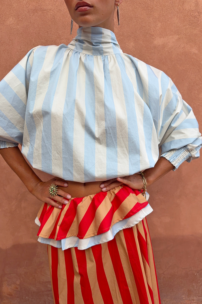 Blue Stripe Batwing Blouse with a high neck and shirred cuffs, paired with a red and tan striped ruffled skirt.