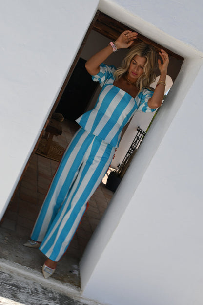 Blue Stripe Kiki peplum top and matching wide-leg trousers on a model in a white doorway on vacation.
