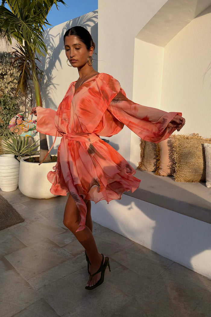 Peach orange Blurred Floral Ella Mini Dress with tiered ruffles and flute sleeves, styled on a model in the sun.