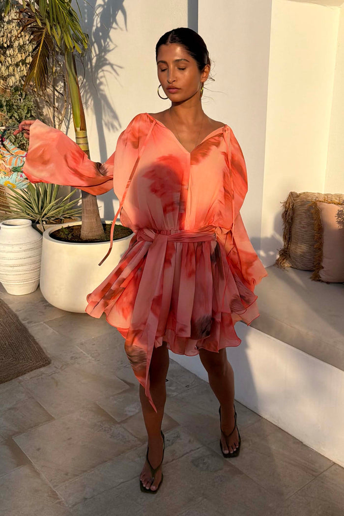 Blurred Floral Ella Mini Dress in peach orange with tiered ruffles and flute sleeves, styled outdoors.