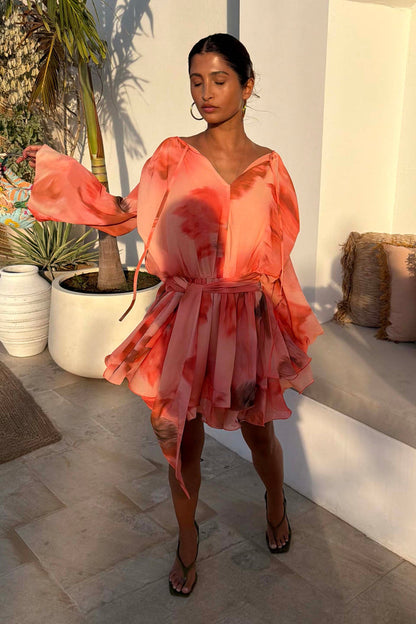Blurred Floral Ella Mini Dress in peach orange with tiered ruffles and flute sleeves, styled outdoors.