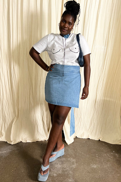 White Boob T-shirt styled with a denim wrap mini skirt and platform wedge sandals on a model.