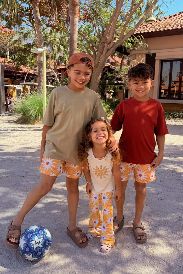 Yellow Sun Swim Shorts and matching sun-print trousers on children in a sandy beach vacation setting.