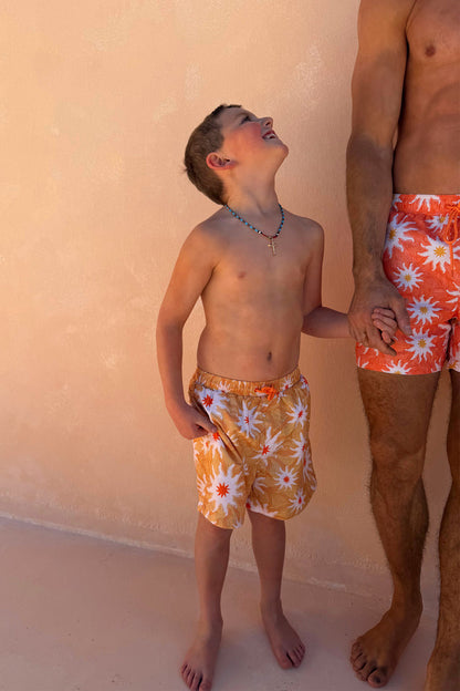 Yellow Sun Kids Swim Shorts in a sun print, worn by a boy holding hands with a man in matching swimwear.