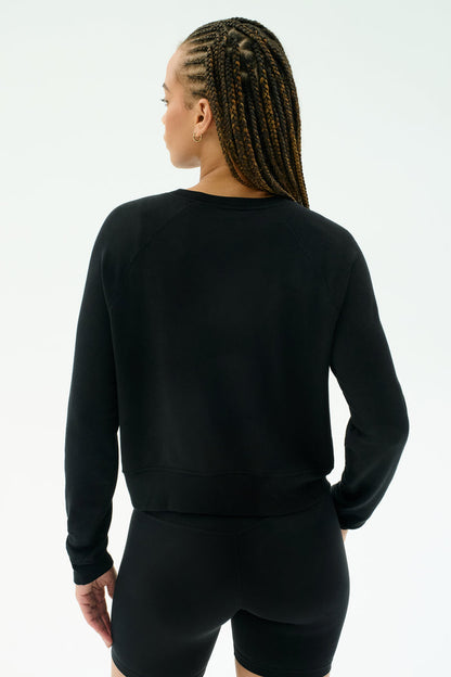 Person with braided hair wears the SPLITS59 Brooks Fleece Long Sleeve Sweatshirt in black, facing away from the camera against a plain light background. Made in Los Angeles for everyday comfort and effortless style.