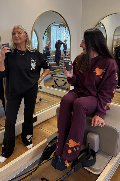 Burgundy cotton wide leg pants with coral embroidery and a matching hoodie for a gym co-ord in a pilates studio.