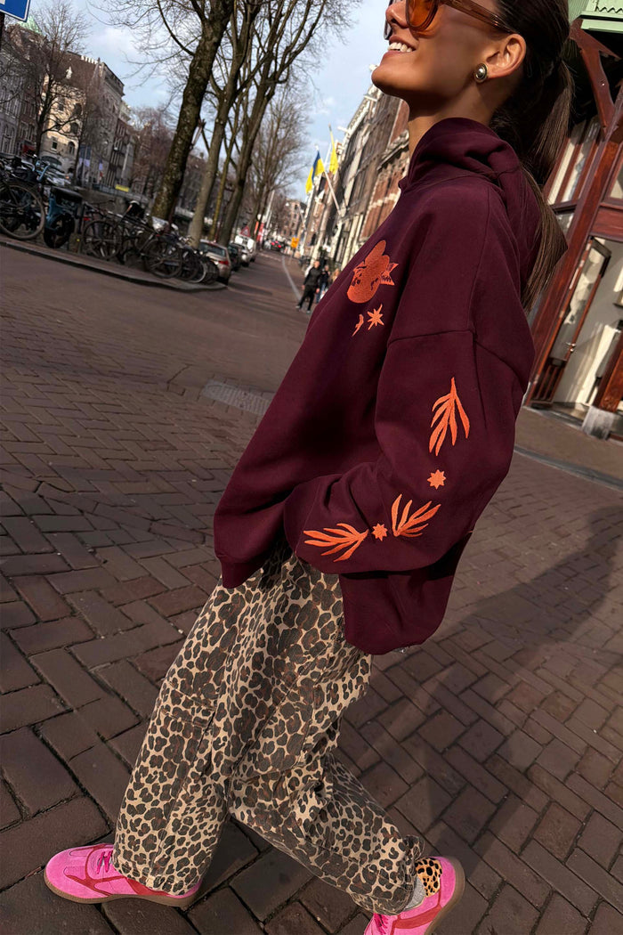 Burgundy Hoodie with Coral Embroidery, styled with leopard print trousers and pink trainers on a city street.