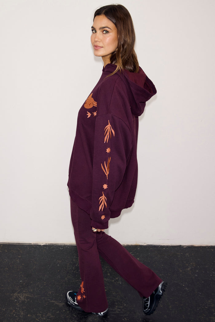Burgundy hoodie with coral embroidery on the sleeve and matching wide-leg leggings on a model.