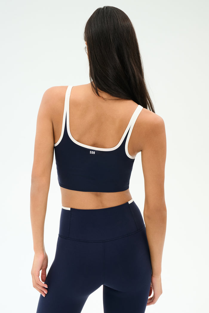 A woman is shown from the back wearing the SPLITS59 Cait Rigor Bralette in Indigo/White, paired with matching high-waisted leggings, both crafted from a soft nylon-spandex blend, against a plain background.