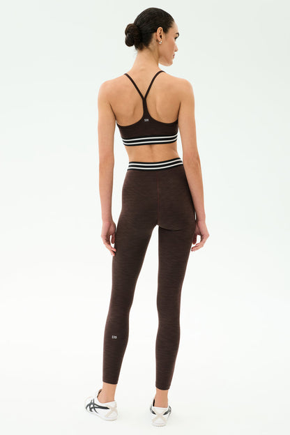 A person stands with their back to the camera, wearing the SPLITS59 Cali Active Rib Bra in Heather Dark Chocolate with matching high-waisted leggings, set against a plain white background.