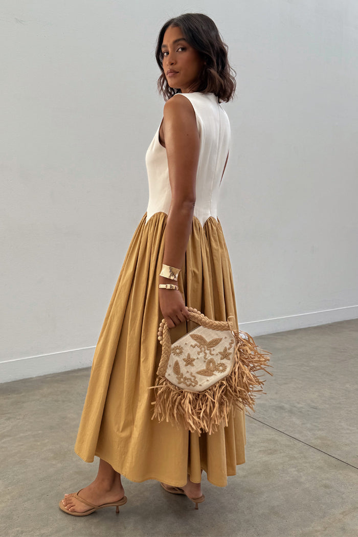 Camel Monika Dress with a cream corset-style top and pleated camel midaxi skirt, styled with a straw bag.