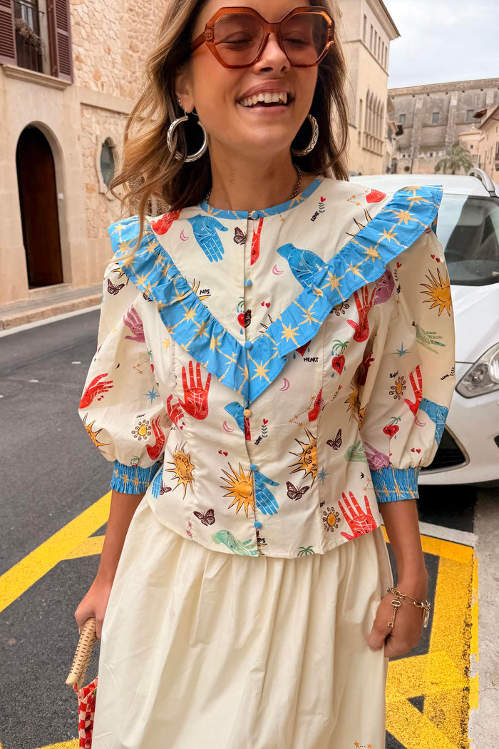 Celestial Nia Top in cream cotton featuring celestial motifs, blue ruffle shoulders and button-up front.