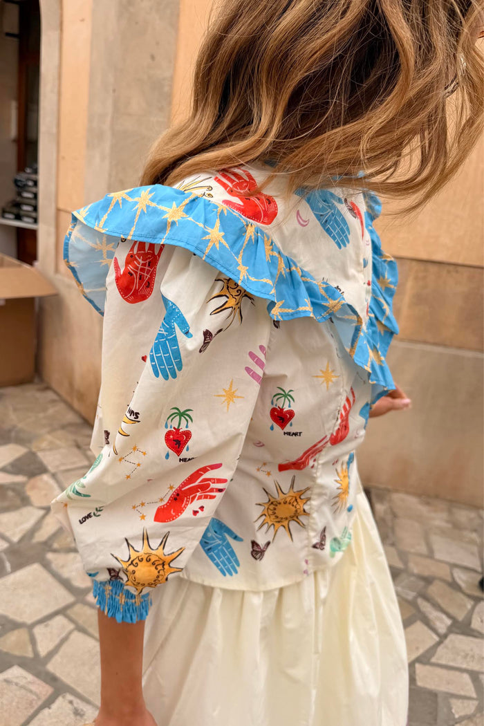Celestial Nia Top in cream cotton with a sun and star print, blue ruffled shoulders and elasticated cuffs.