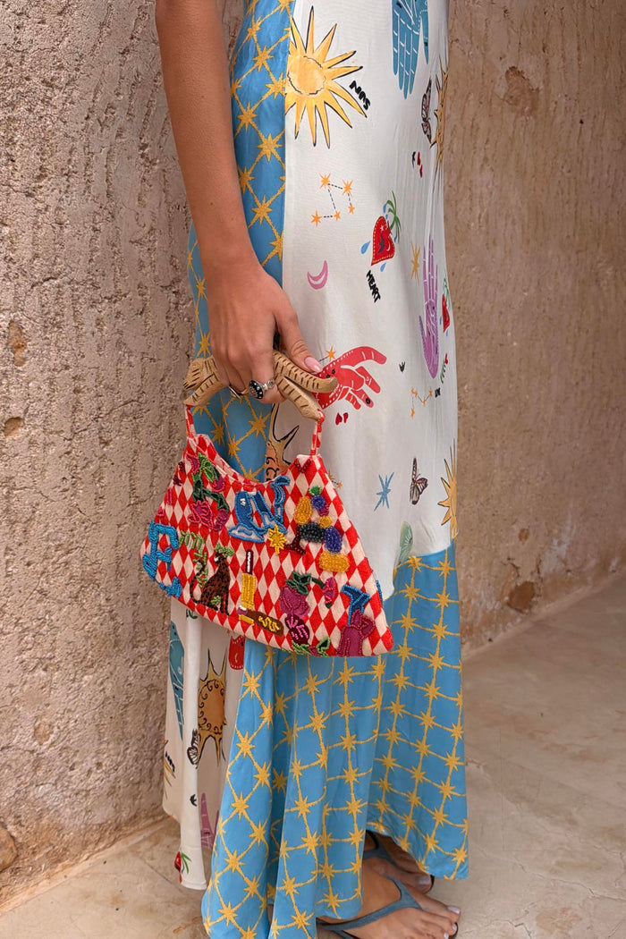 Multi-wear Celestial Patti Dress with sun and star motifs, paired with a beaded red and white diamond-patterned bag.