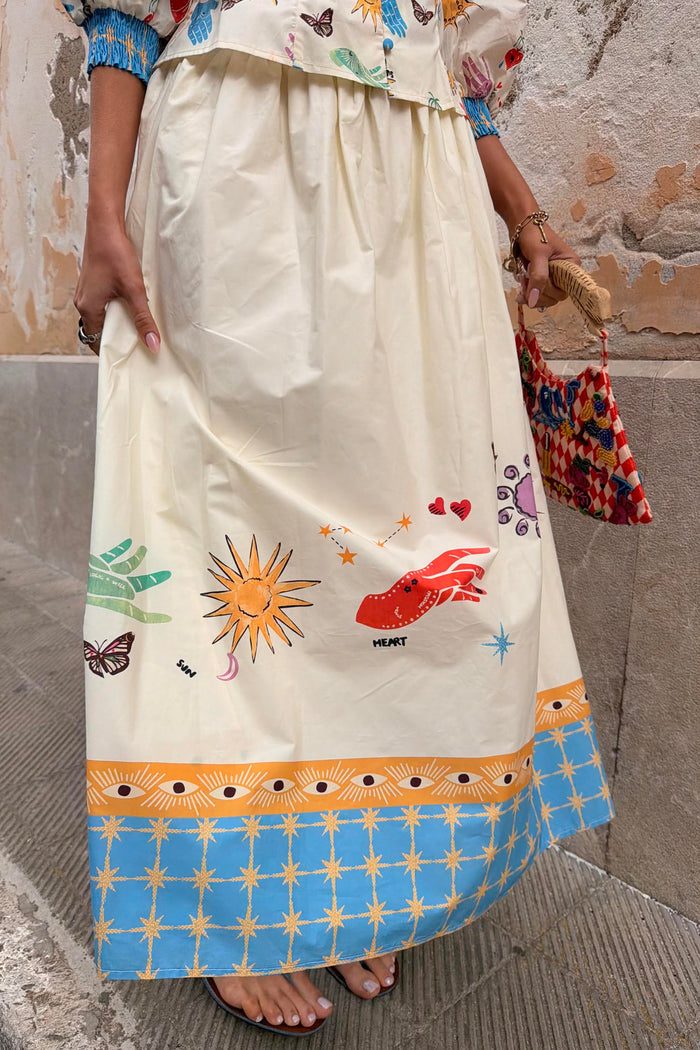 Celestial Talia Skirt in cream cotton with sun and palm motifs and a blue border featuring stars and eye designs.
