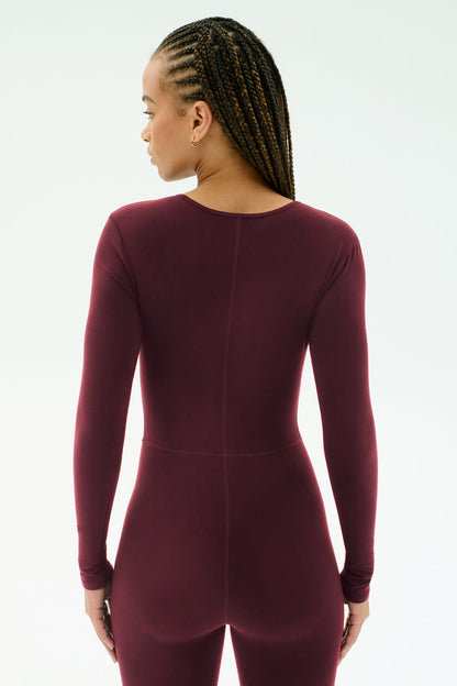 A person with braided hair models the SPLITS59 Chloe Airweight Jumpsuit in Dark Cherry, standing with their back to the camera against a plain light background.