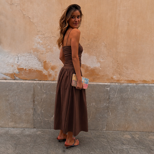Chocolate Lola Mid-axi Dress in brown cotton with a ruched bodice and thin straps, styled with a clutch.