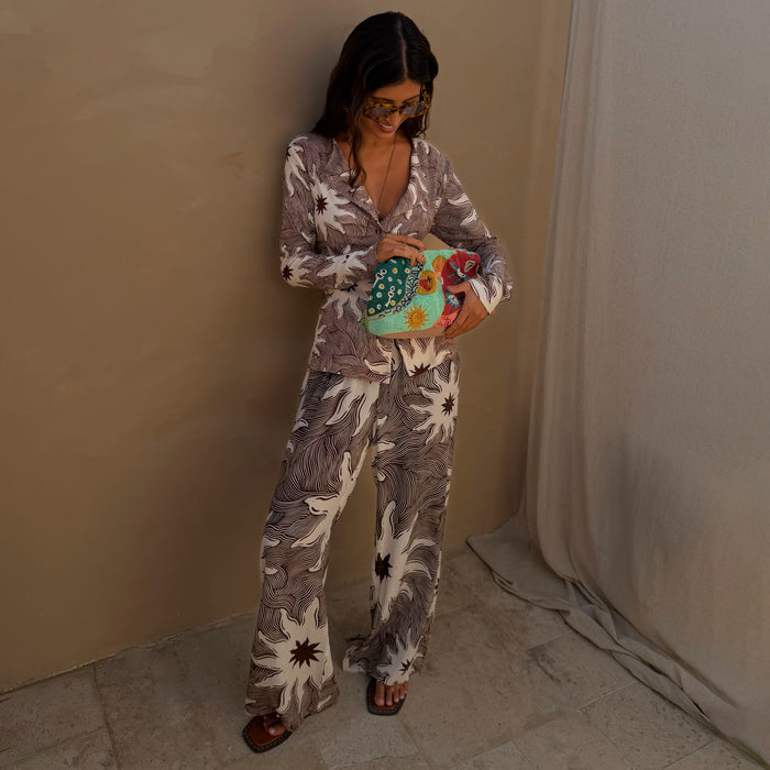 Chocolate Soleil Ellie Trousers and matching cardigan with sun motifs, styled with a colourful beaded clutch bag.