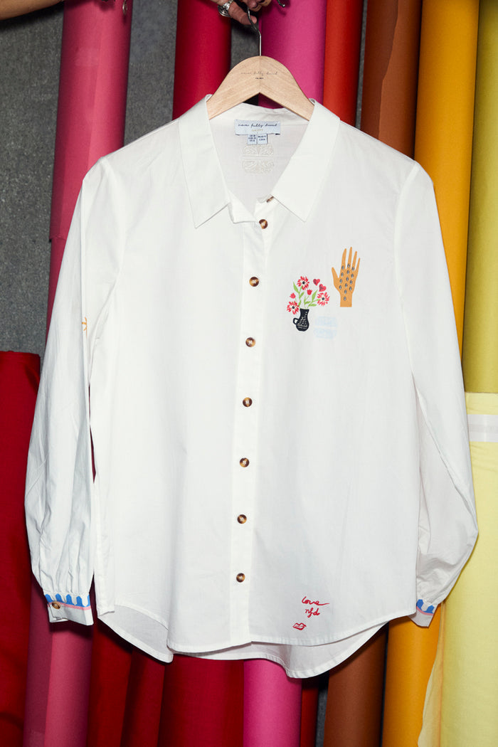 White cotton Choose Love Miley Shirt with colourful chest graphics and patterned cuffs, hanging in a studio.
