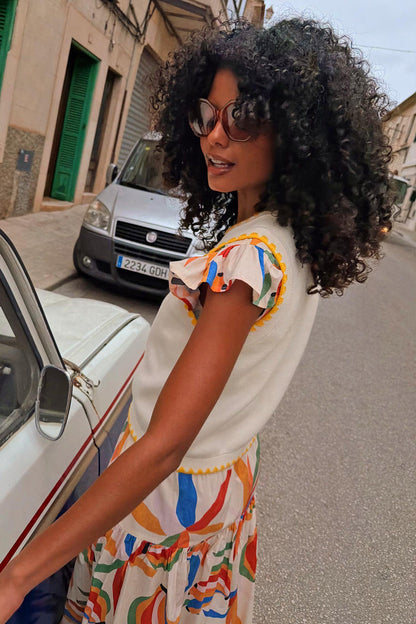 Cream knit Banana Tank with yellow contrast stitching, layered over a colourful abstract print skirt on a city street.