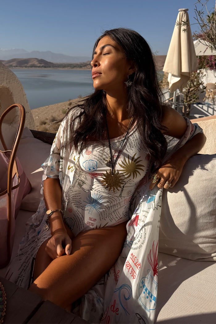 Cream Palma One Shoulder Swimsuit with hand-painted sun motifs and crochet trim, styled with a matching robe.