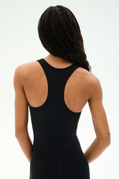 A person with long braided hair models the SPLITS59 Darci Airweight Stirrup Jumpsuit in black, shown from behind against a plain light background.