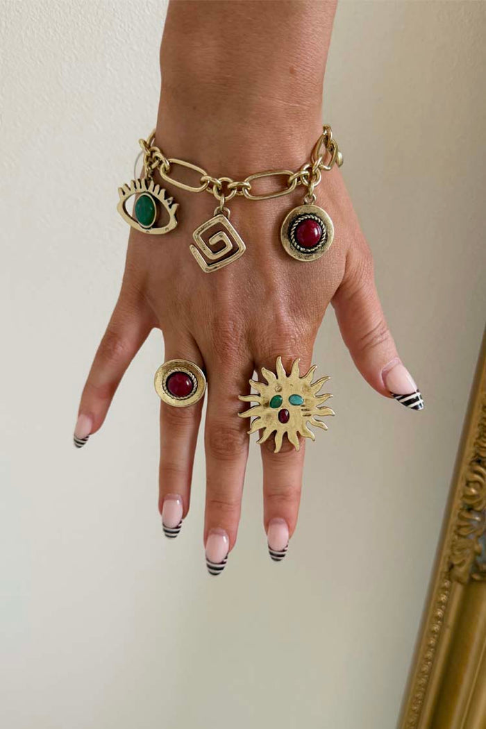 Brushed gold Deloris Charm Bracelet with eye and stone charms, styled on a hand with matching sun and stone rings.