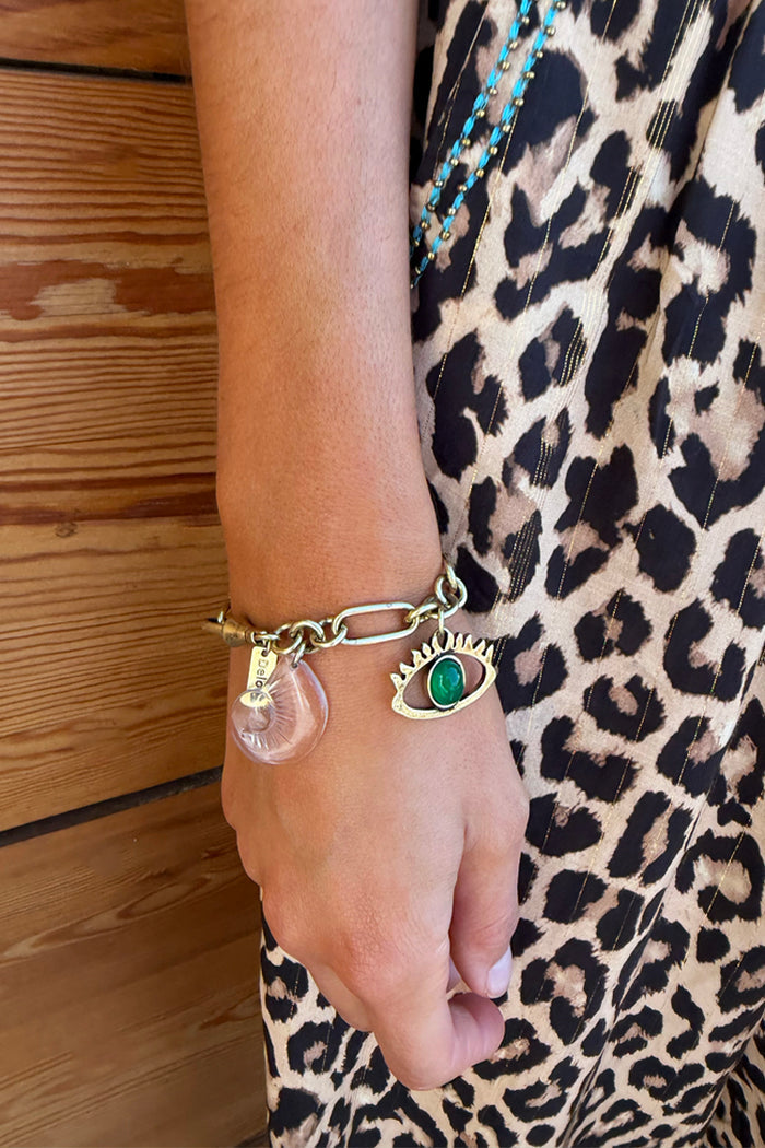 Deloris Charm Bracelet in brushed gold with eye and mermaid charms, worn with a leopard print dress.