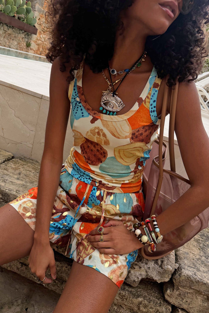 Deloris Eye Necklace with a metal eye motif and blue stones, styled over a colourful seashell print co-ord.