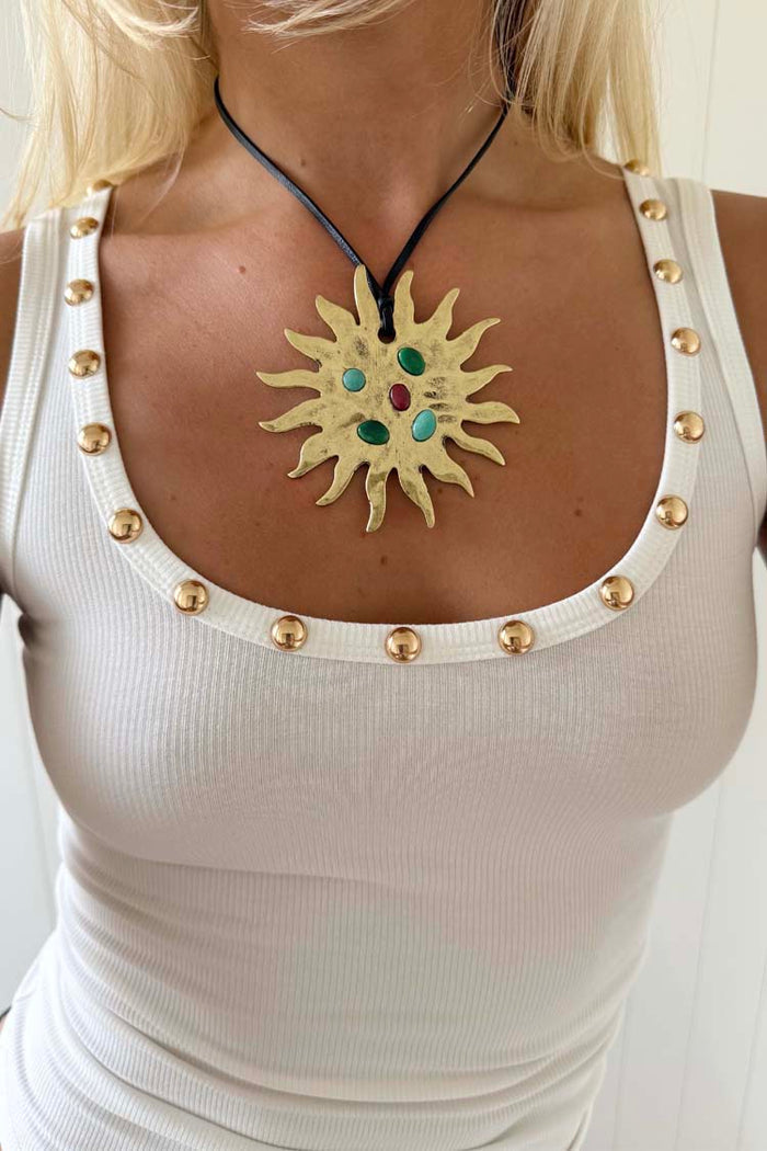 Deloris Sun Necklace featuring a gold sun pendant with semi-precious stones on a black leather cord and white vest top.