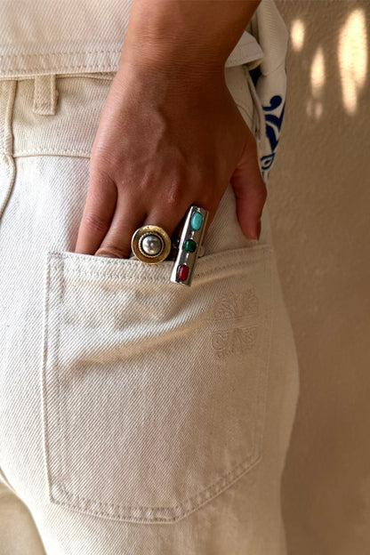 Deloris Whistle Ring with turquoise, green and red gemstones on a chunky silver-toned band, styled on a hand in a pocket.