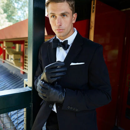 Man in a black tuxedo with gloves standing against a blurred background