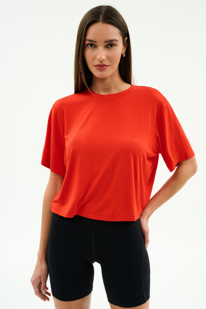 A person models the SPLITS59 Djuna Oversized Jersey Tee in Lotus Red with black shorts against a plain white background, perfect for outdoor or gym workouts.