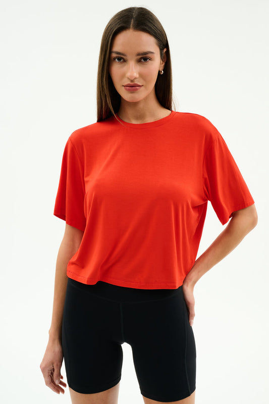 A person models the SPLITS59 Djuna Oversized Jersey Tee in Lotus Red with black shorts against a plain white background, perfect for outdoor or gym workouts.