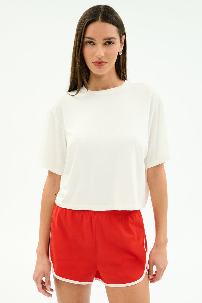 A person faces forward against a white background, wearing the SPLITS59 Djuna Oversized Jersey Tee in white and red athletic shorts with white trim.