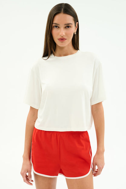 A person faces forward against a white background, wearing the SPLITS59 Djuna Oversized Jersey Tee in white and red athletic shorts with white trim.