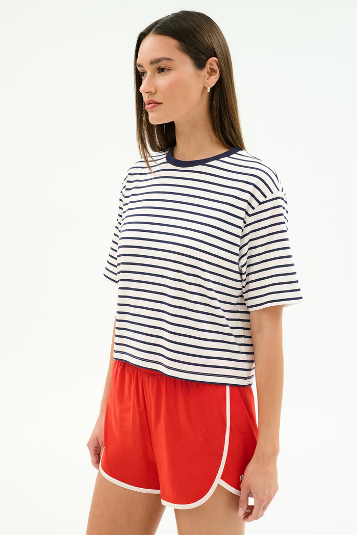 A woman wears the SPLITS59 Djuna Oversized Jersey Tee in White/Indigo Stripe with red athletic shorts, standing against a plain white background.