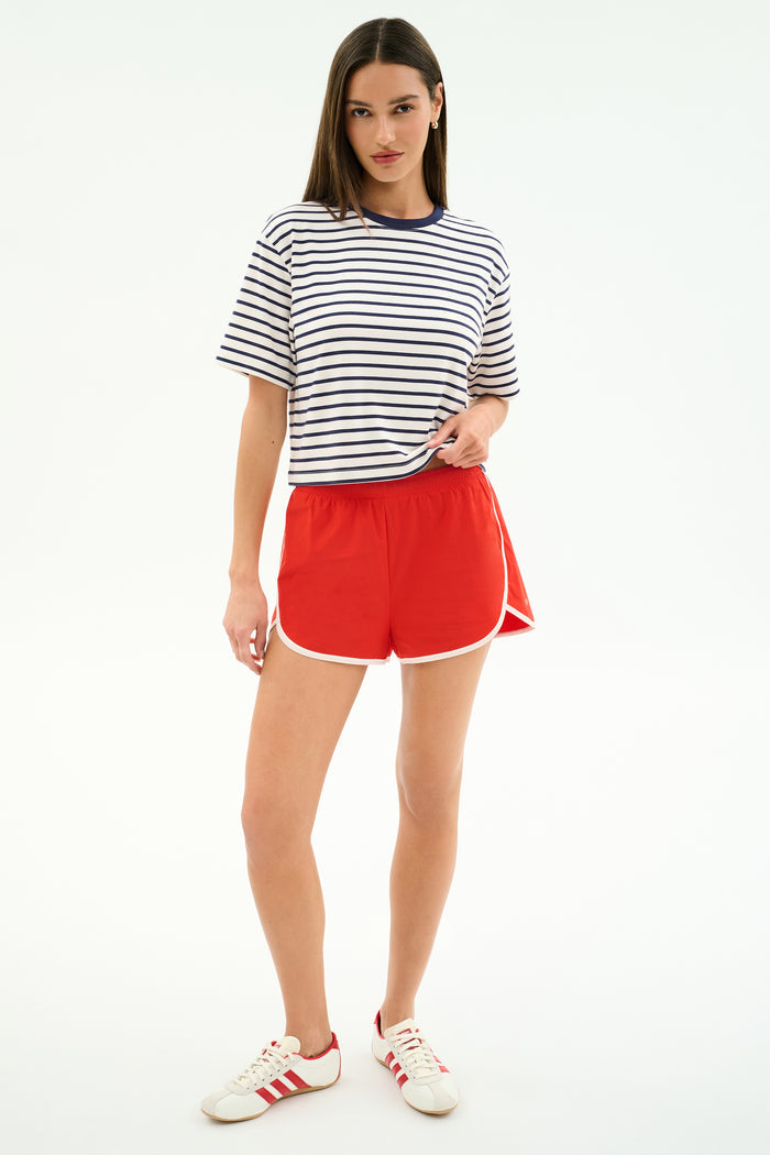 A woman wears the SPLITS59 Djuna Oversized Jersey Tee in White/Indigo Stripe, styled with red athletic shorts and white sneakers with red accents—ideal for gym workouts—against a plain white backdrop.