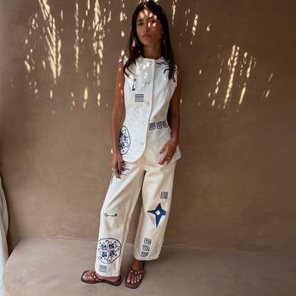 Cream Dolce Vita embroidered denim barrel leg jeans with blue motifs, worn with a matching waistcoat.
