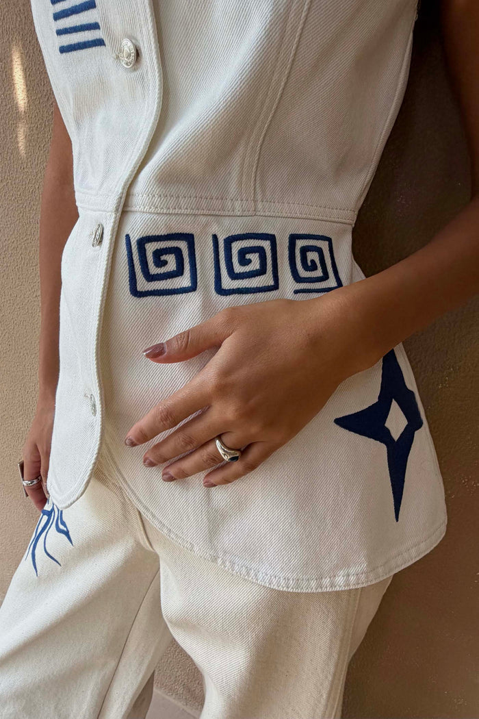 Dolce Vita ecru denim waistcoat featuring blue Greek embroidery and engraved metal buttons.