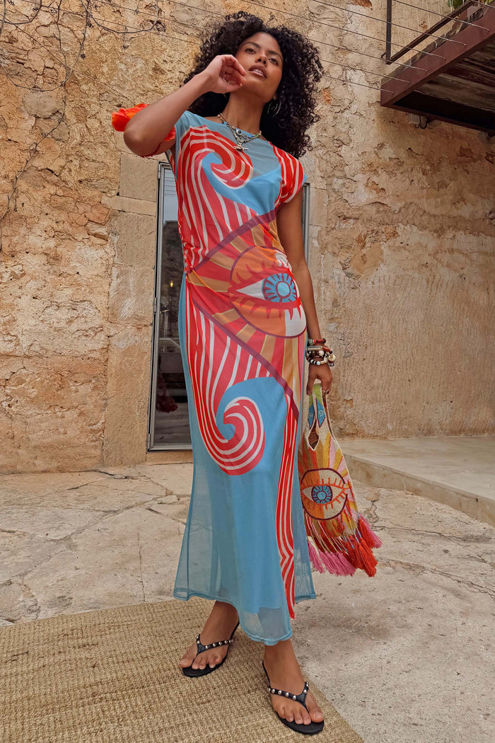 Dolce Vita Mesh Dress in blue with red swirl and eye motifs on a model in a vacation setting.
