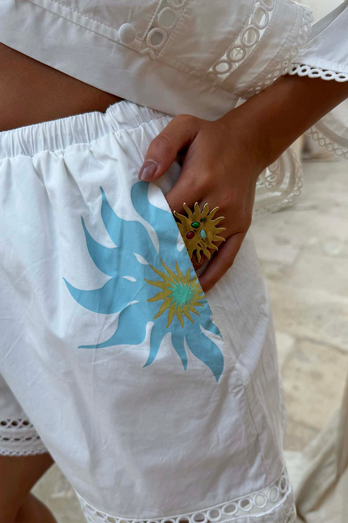 White cotton Dreamer Ellie Shorts featuring a blue sun motif and circular cut-out hem detailing.