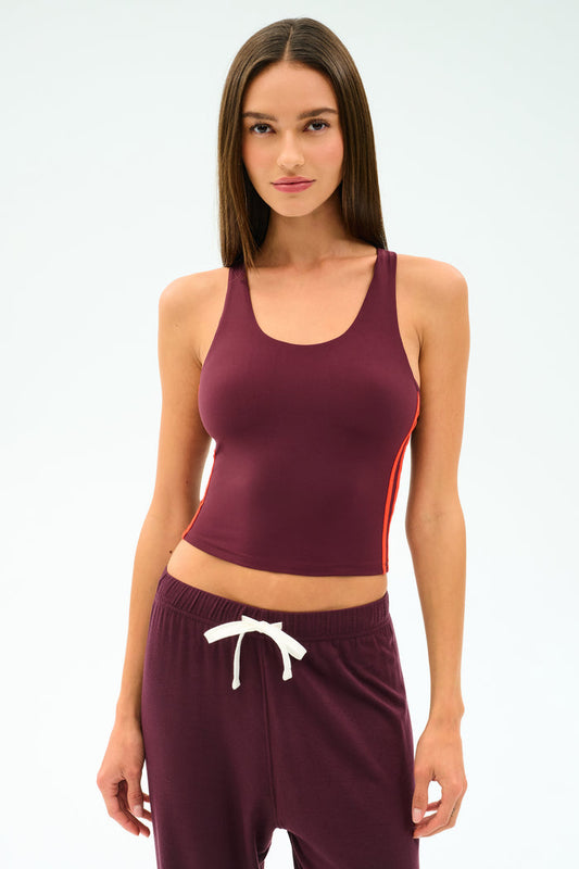 A woman stands against a plain light background wearing the SPLITS59 Ella Airweight Tank in Dark Cherry/Valencia, paired with matching sweatpants featuring a white drawstring, both crafted from stretchy nylon spandex fabric.