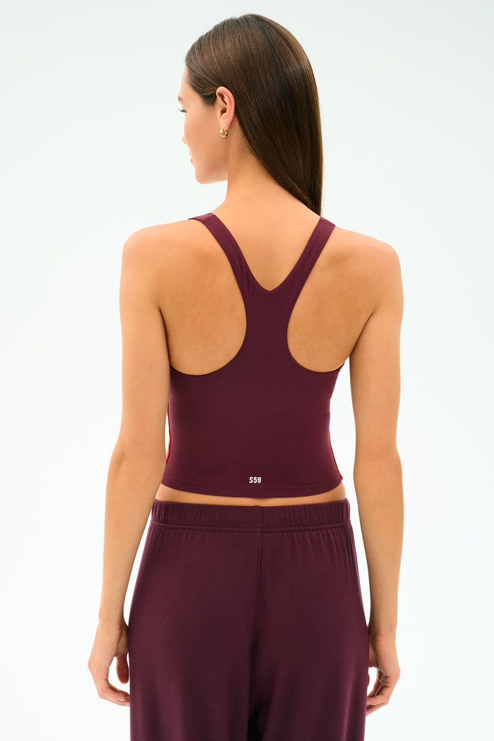A woman with straight brown hair is seen from the back, wearing the SPLITS59 Ella Airweight Tank in Dark Cherry/Valencia, paired with matching pants, against a plain light background.