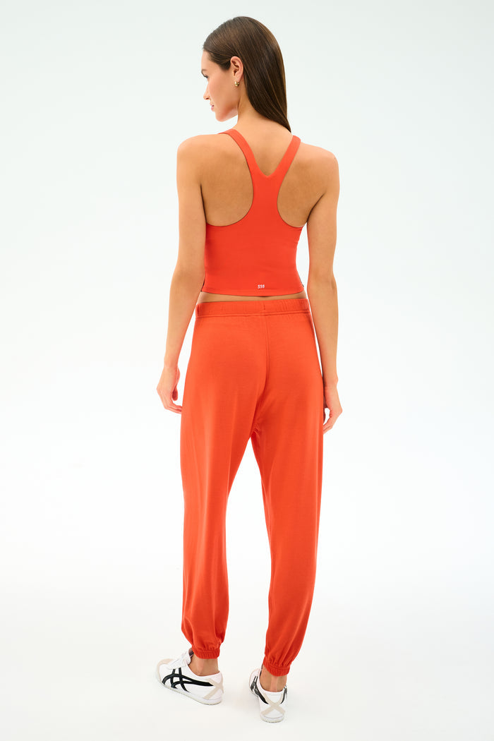 A woman stands with her back to the camera in the SPLITS59 Ella Airweight Tank in Valencia/Indigo, paired with matching stretch jogger pants and white sneakers, against a plain white background.