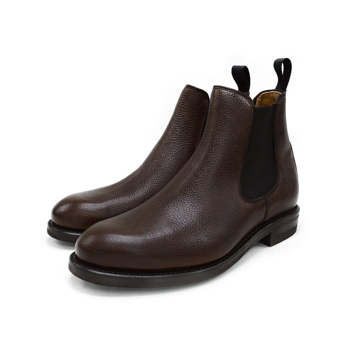 A dark brown grain leather Chelsea boot with a black elastic side panel and a round toe. The boot has a low heel and a goodyear welted dainite rubber sole.
