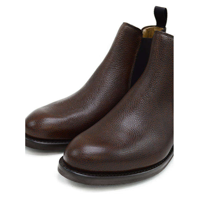 A dark brown grain leather Chelsea boot with a black elastic side panel and a round toe. The boot has a low heel and a goodyear welted dainite rubber sole.