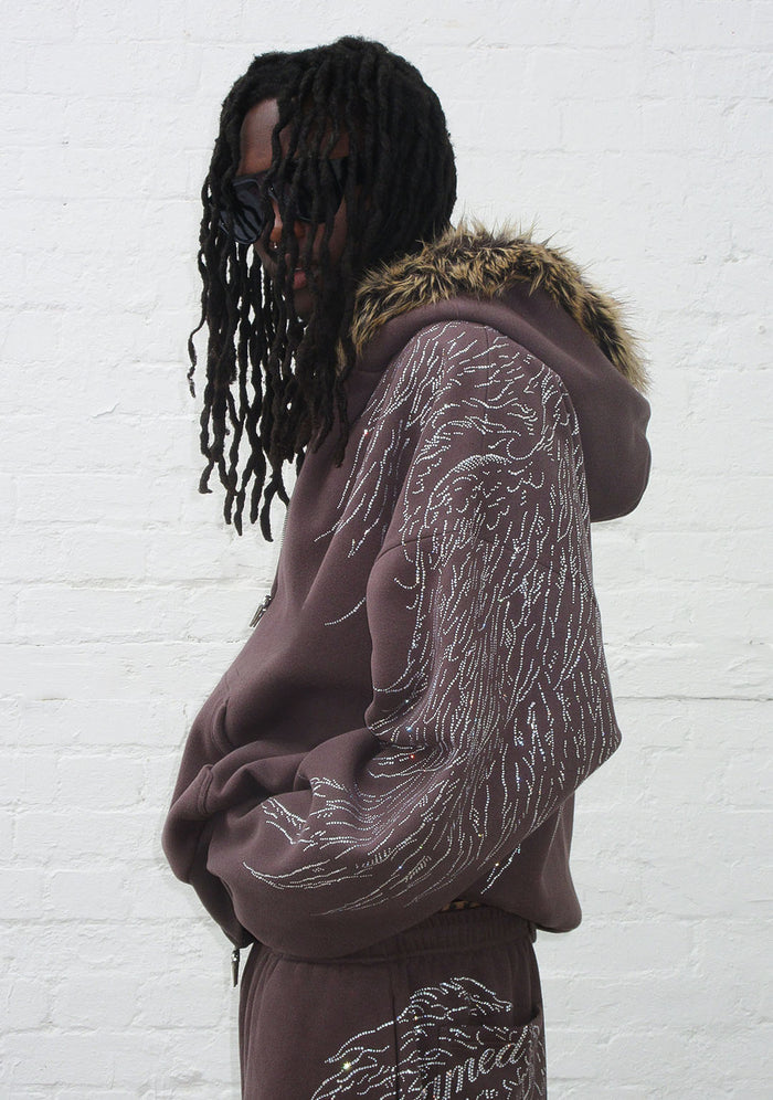 Model wearing a brown hoodie with rhinestone wing design and detachable faux fur hood, viewed from the side.